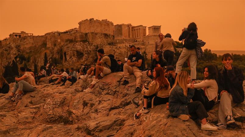 Menschen fotografieren die Akropolis in der dunstig-roten Stimmung des Saharastaubs, 23. April.